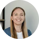 Smiling woman with long light brown hair wearing a blue blazer and white top against a neutral background.