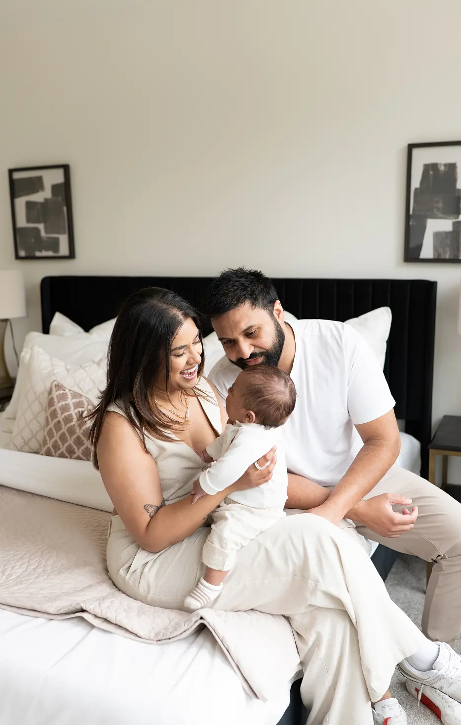 Smiling couple sitting on a bed, holding and looking lovingly at their baby.