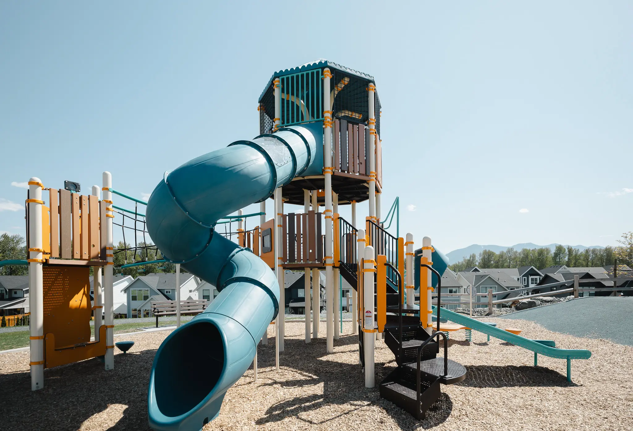 Gravel path winding through lush green trees and foliage alongside a small pond under a partly cloudy blue sky.