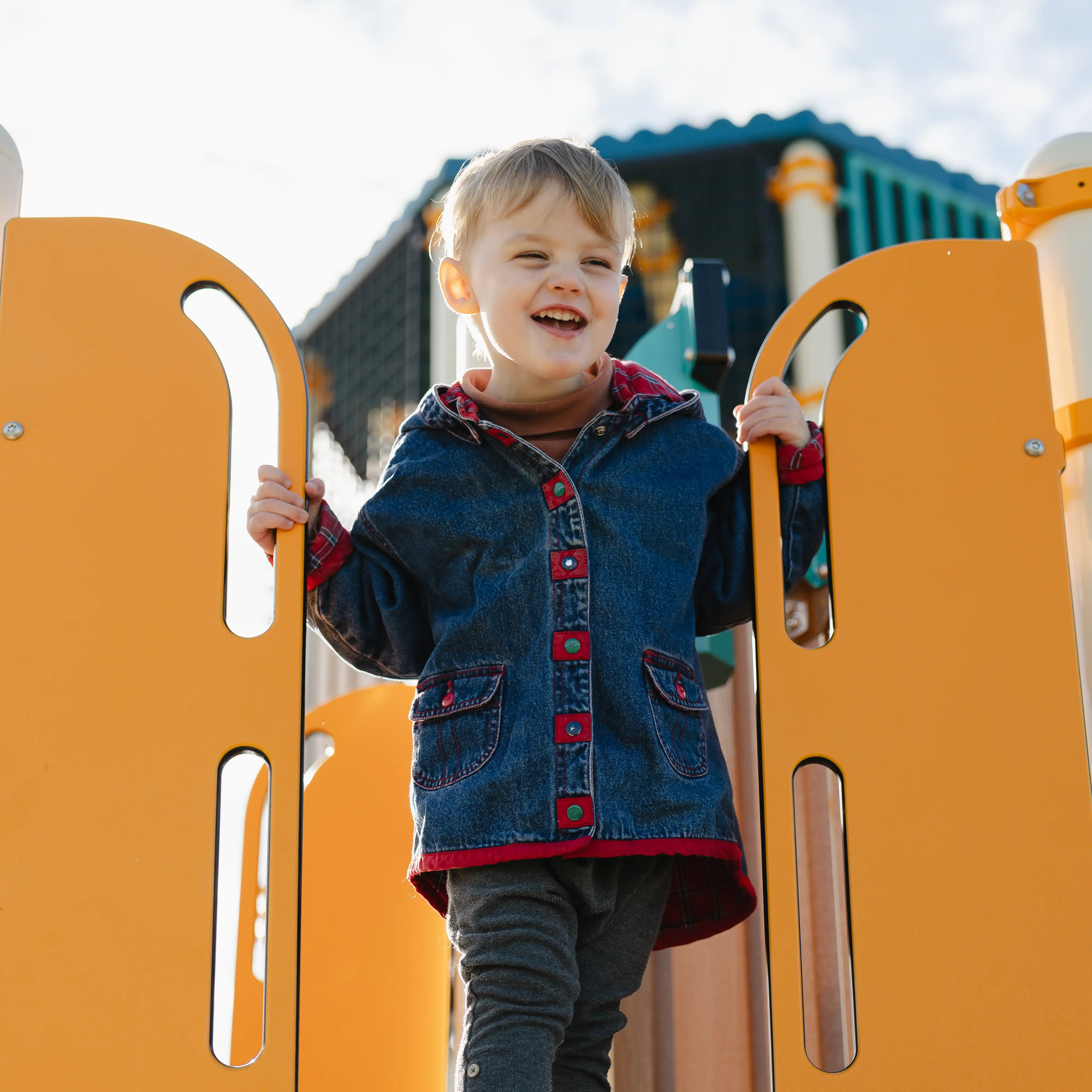 Aerial view of a residential neighborhood with houses lined along a street next to a green forested area and a hill in the background under a clear sky.