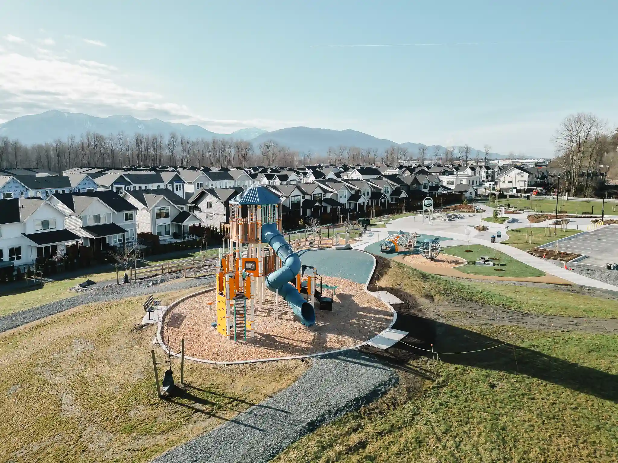 Aerial view of a river winding through autumn-colored trees with a small town and hills in the background under a cloudy sky.