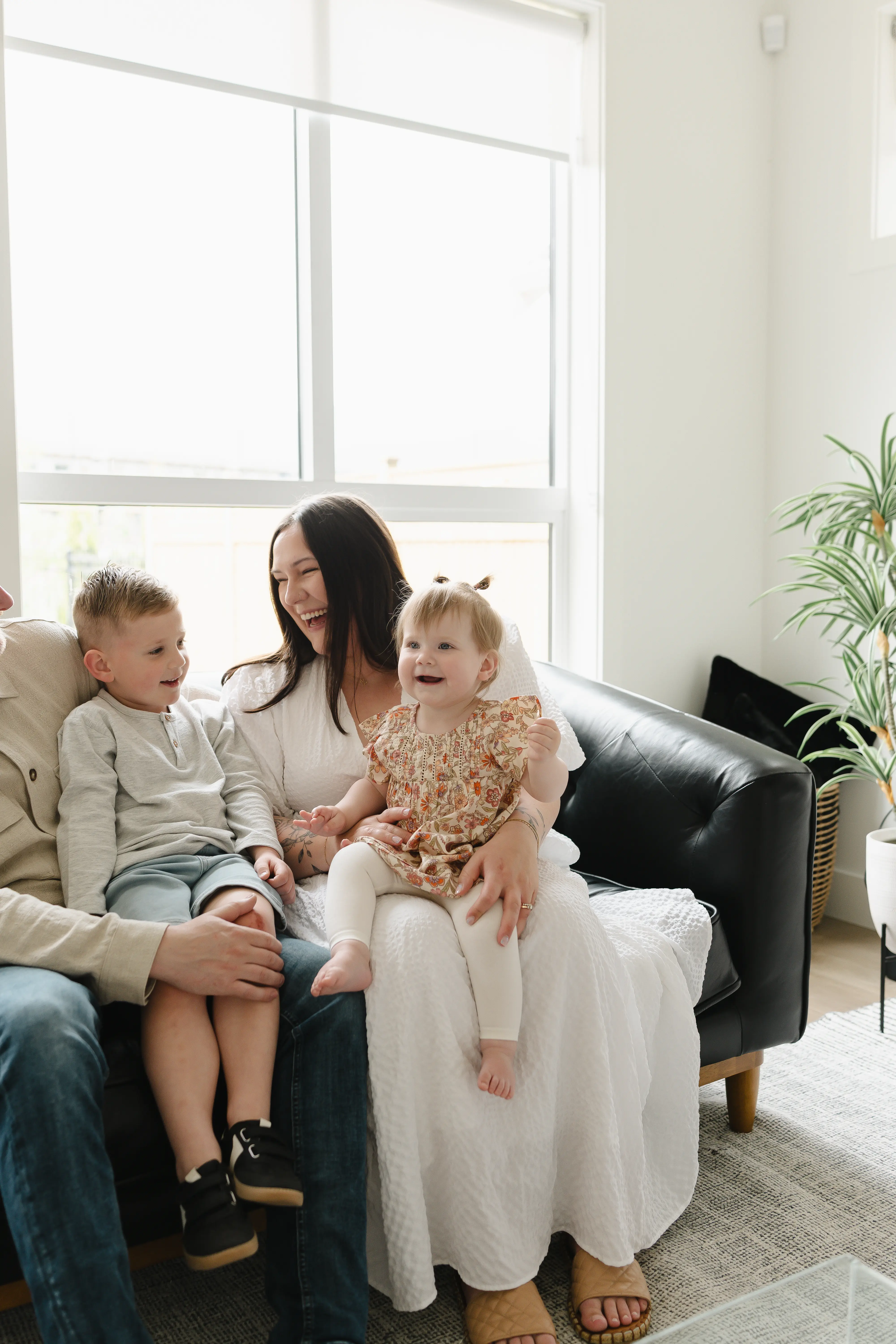 Smiling parents holding and playing with their baby who wears white outfit and striped socks indoors.