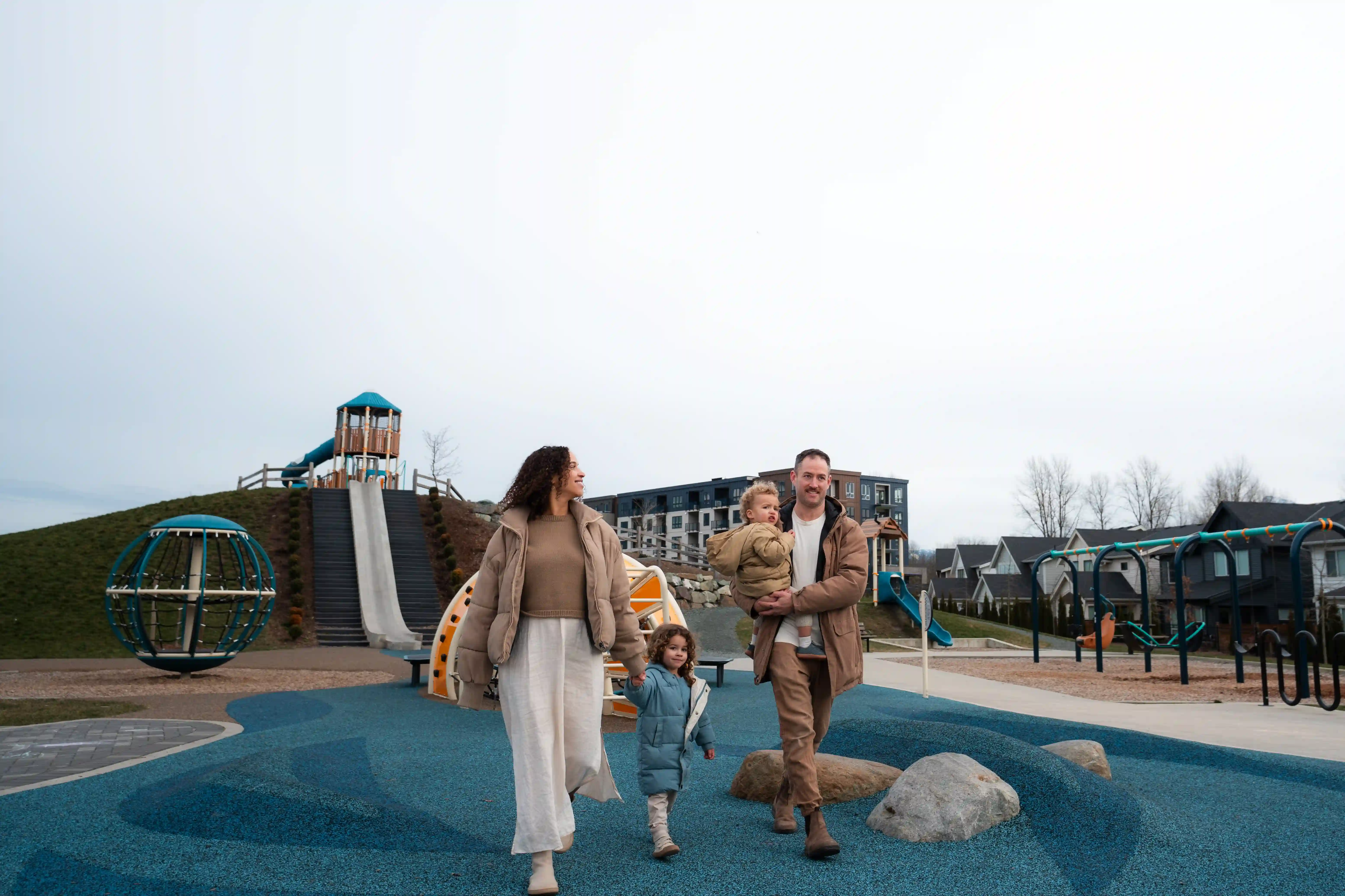 Gravel path winding through lush green trees and foliage alongside a small pond under a partly cloudy blue sky.