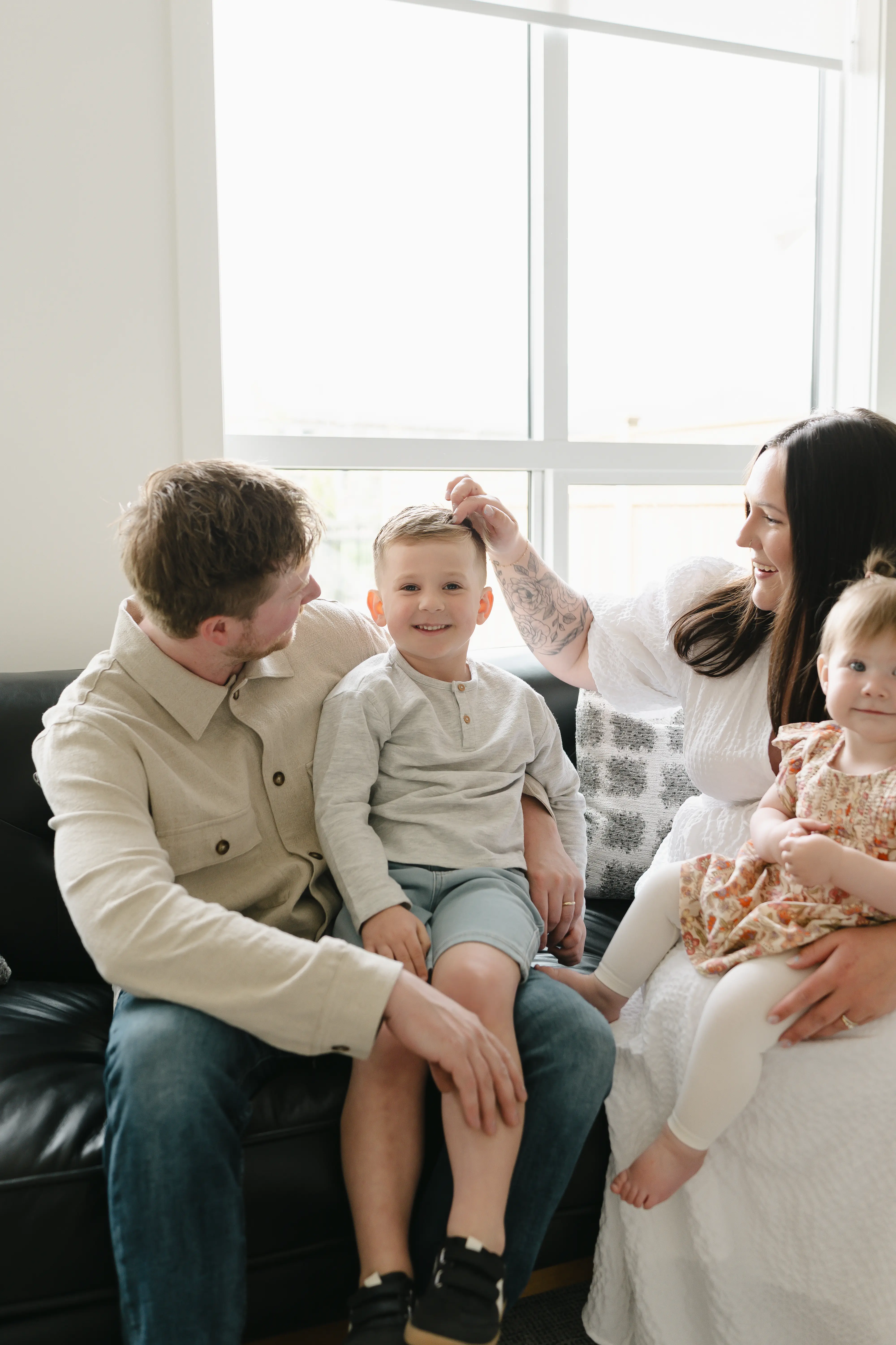 Smiling parents holding and playing with their baby who wears white outfit and striped socks indoors.