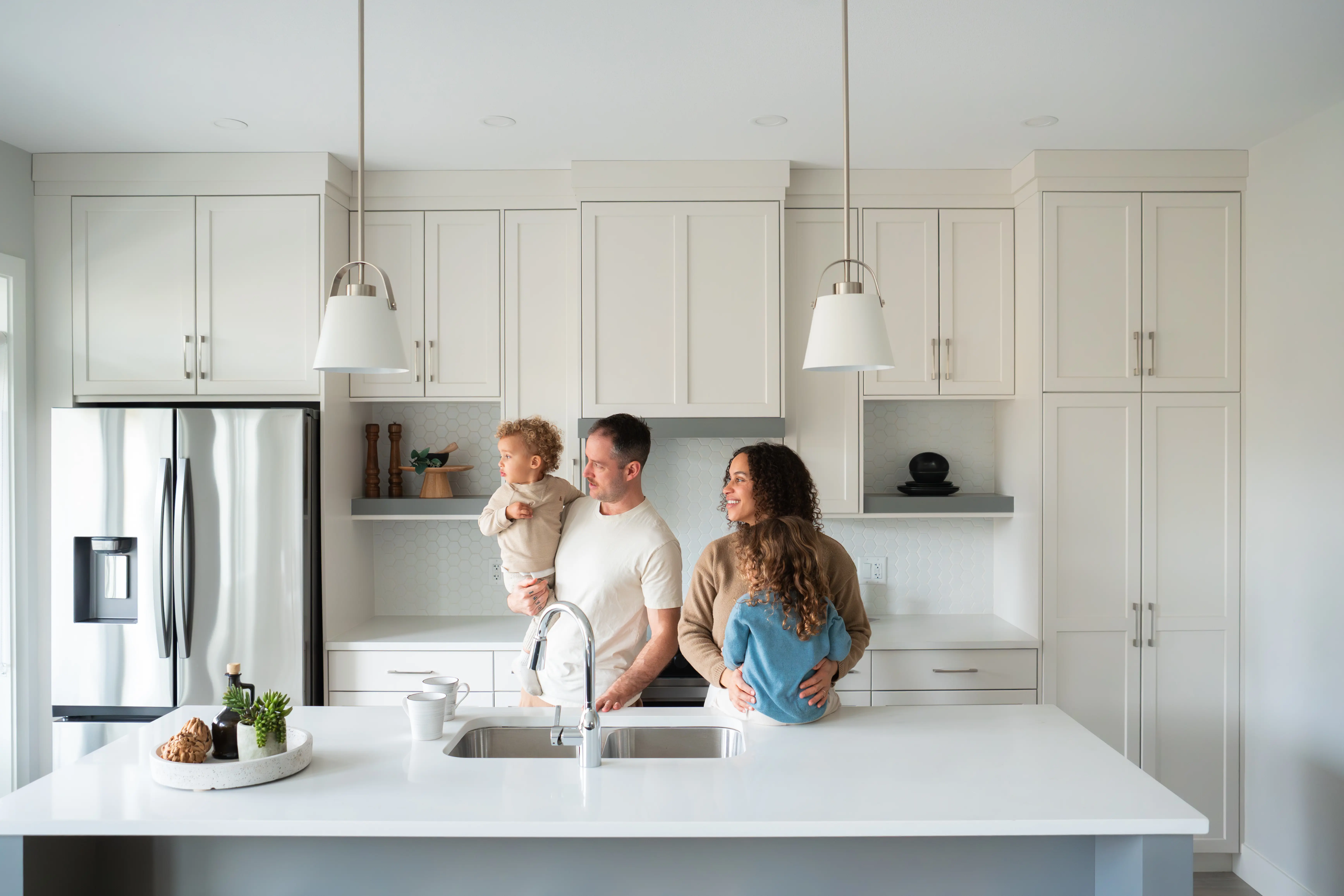 Smiling parents play and laugh with their young child on a white couch in a bright living room.