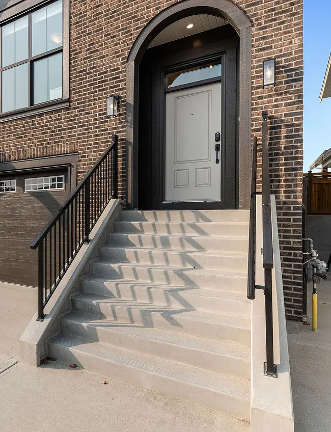 Concrete stairs with black metal railings leading to a white front door set in a brick house facade under a black arched frame.