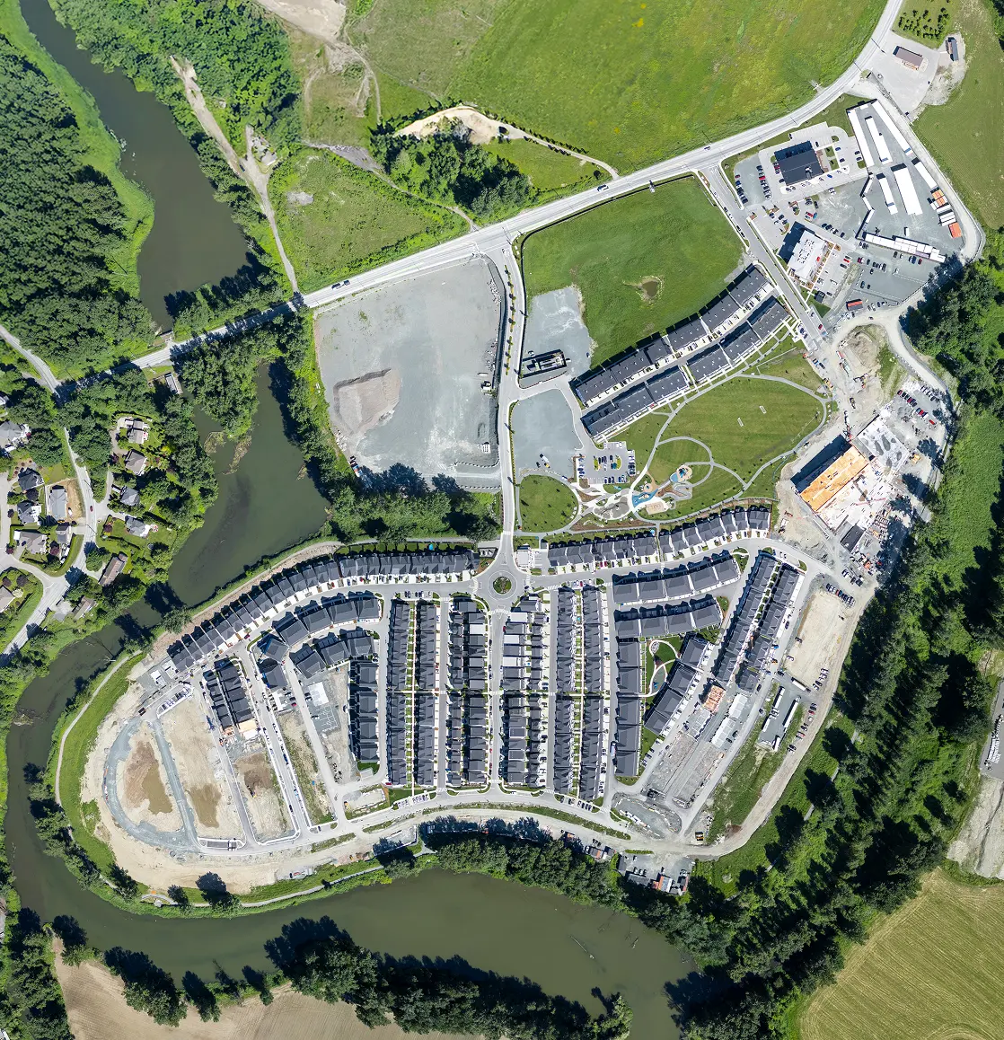 Aerial view of a residential neighborhood with rows of houses, green spaces, a river surrounding the area, and some construction sites.