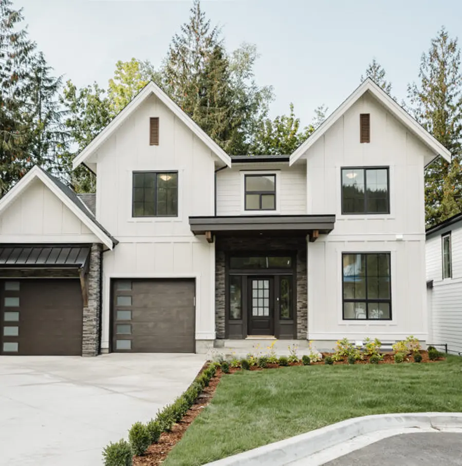 Modern two-story white house with dark-framed windows, double garage doors, and a neatly landscaped green lawn.