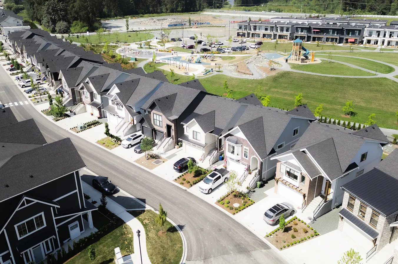 Aerial view of a suburban neighborhood with a row of modern houses along a curved road and a large green park with a playground behind.