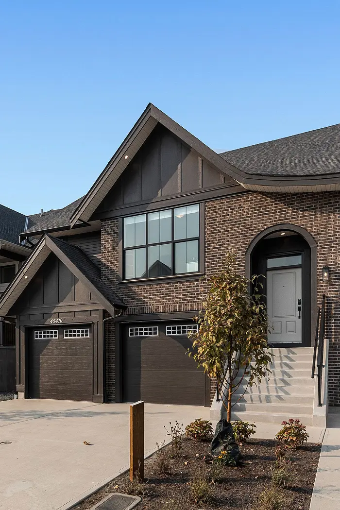 Modern two-story brick house with dark brown garage doors, large front window, and light gray front door accessed by stairs.
