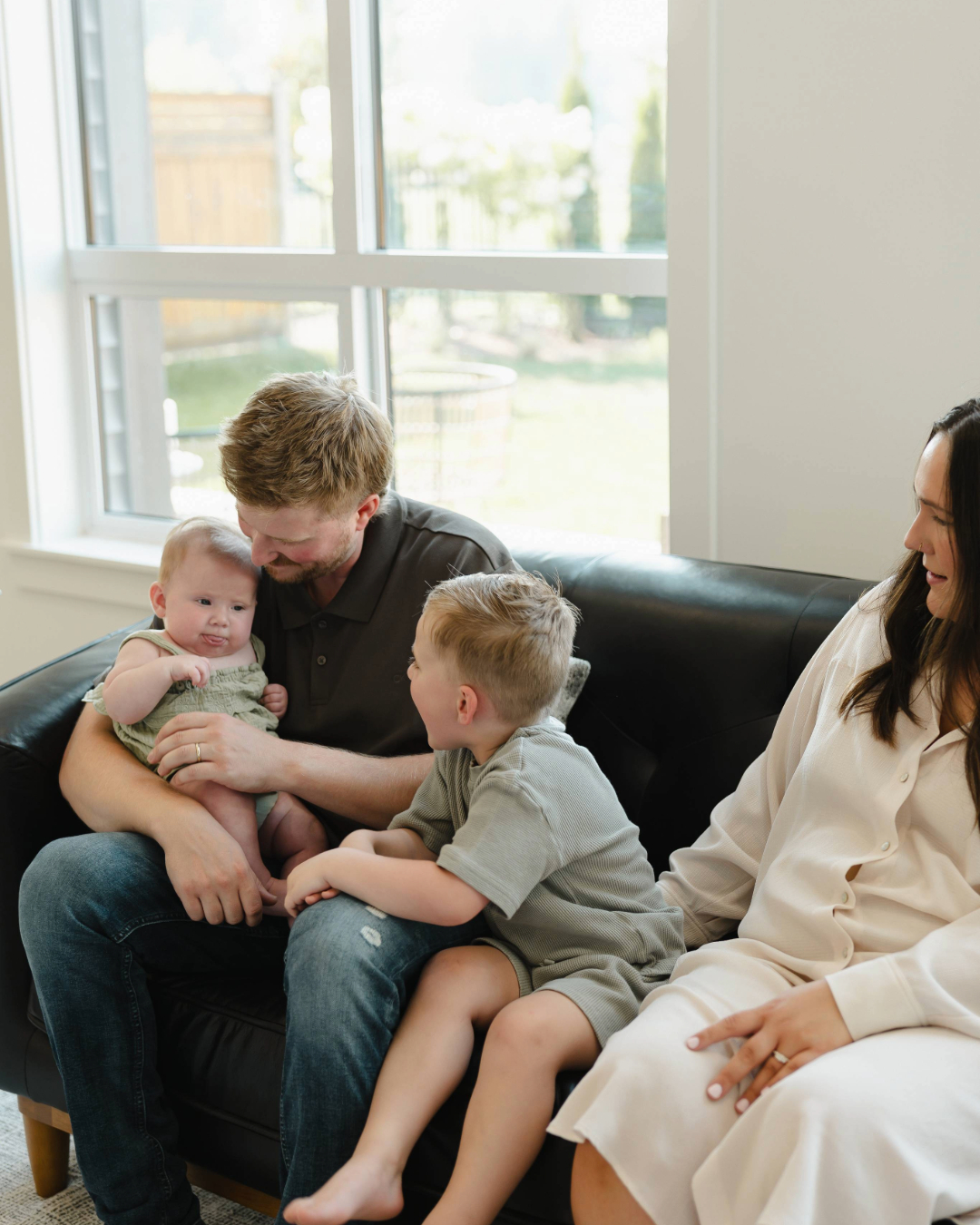 Smiling man with short curly hair and beard wearing a white jacket against a dark background.