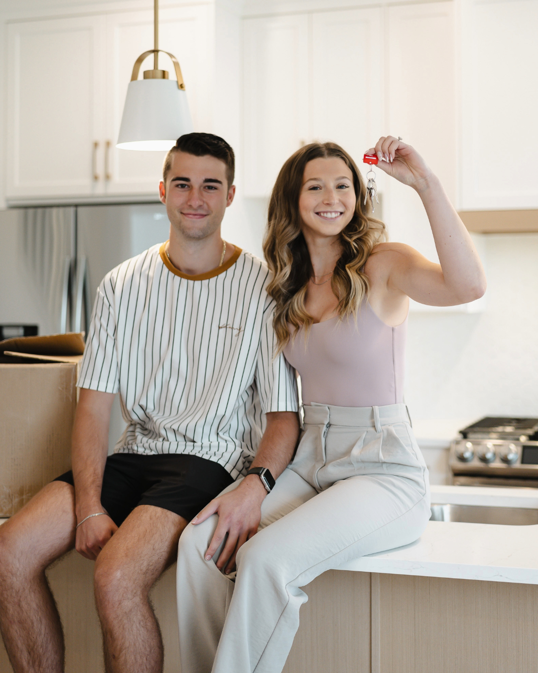 Smiling young couple holding a keyring with several keys in a bright room.
