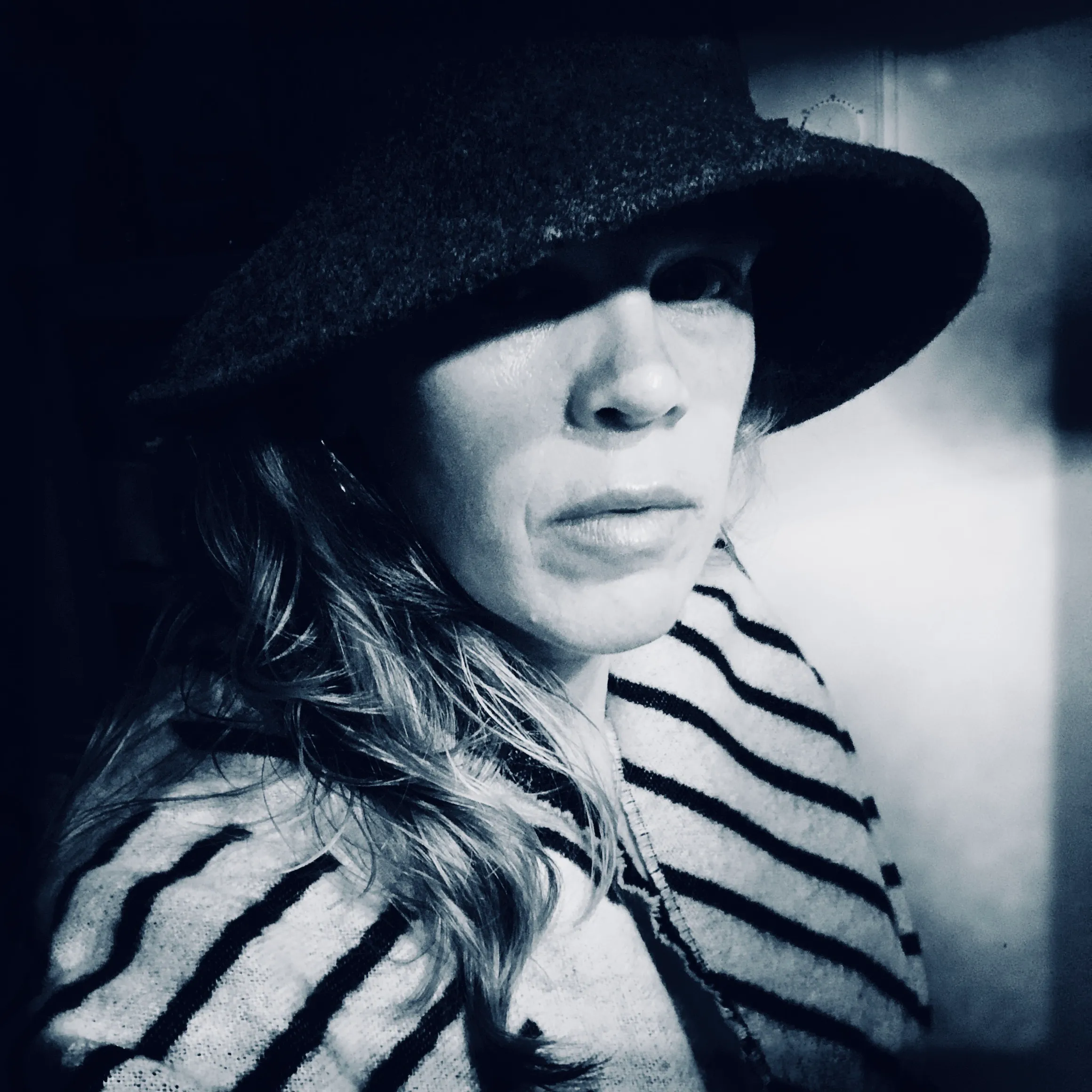 Portrait en noir et blanc d'une femme portant un chapeau large et une couverture rayée.