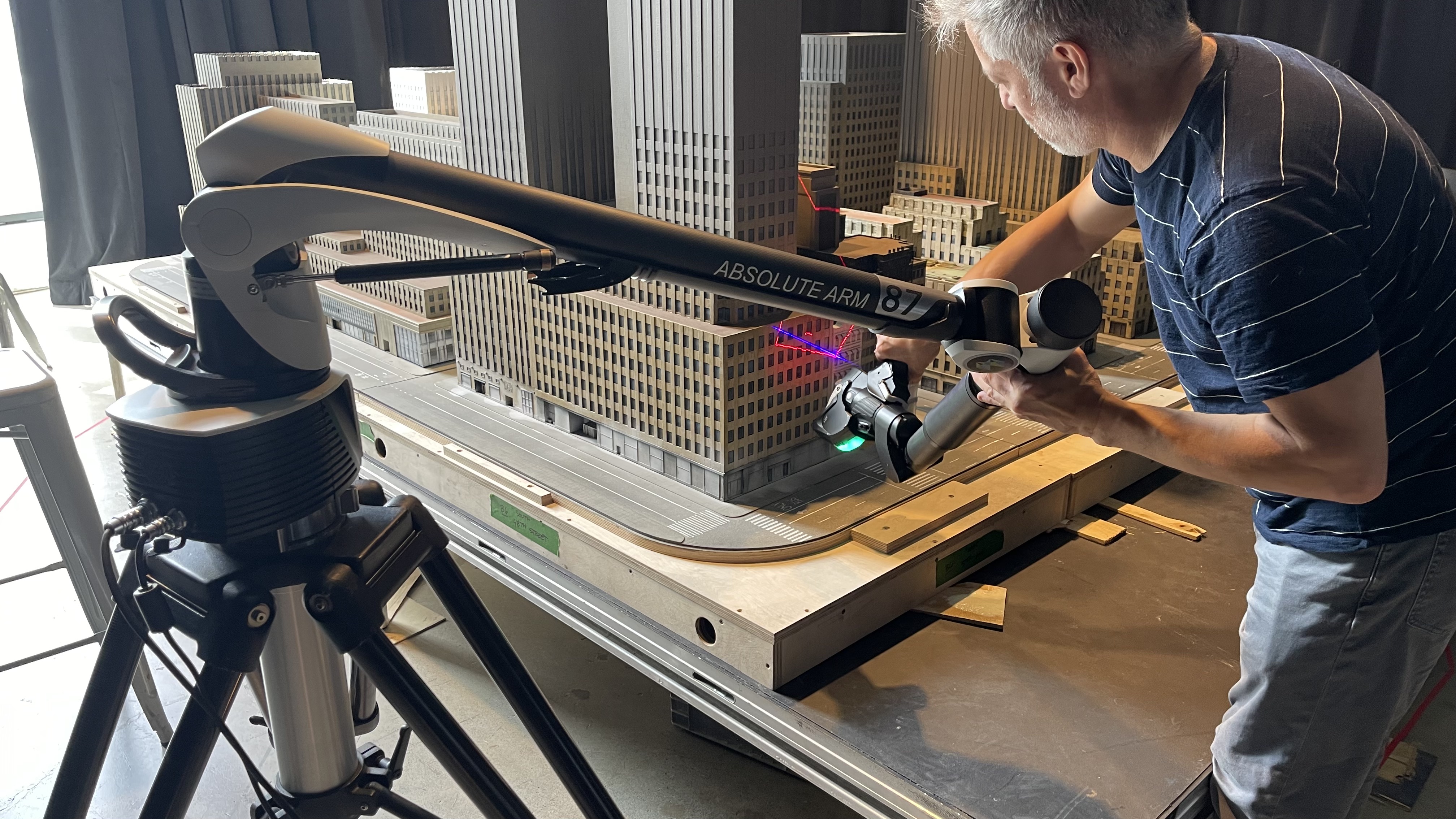 Homme utilisant un bras de mesure ABSOLUTE ARM 87 pour scanner une maquette d'immeubles sur une table.