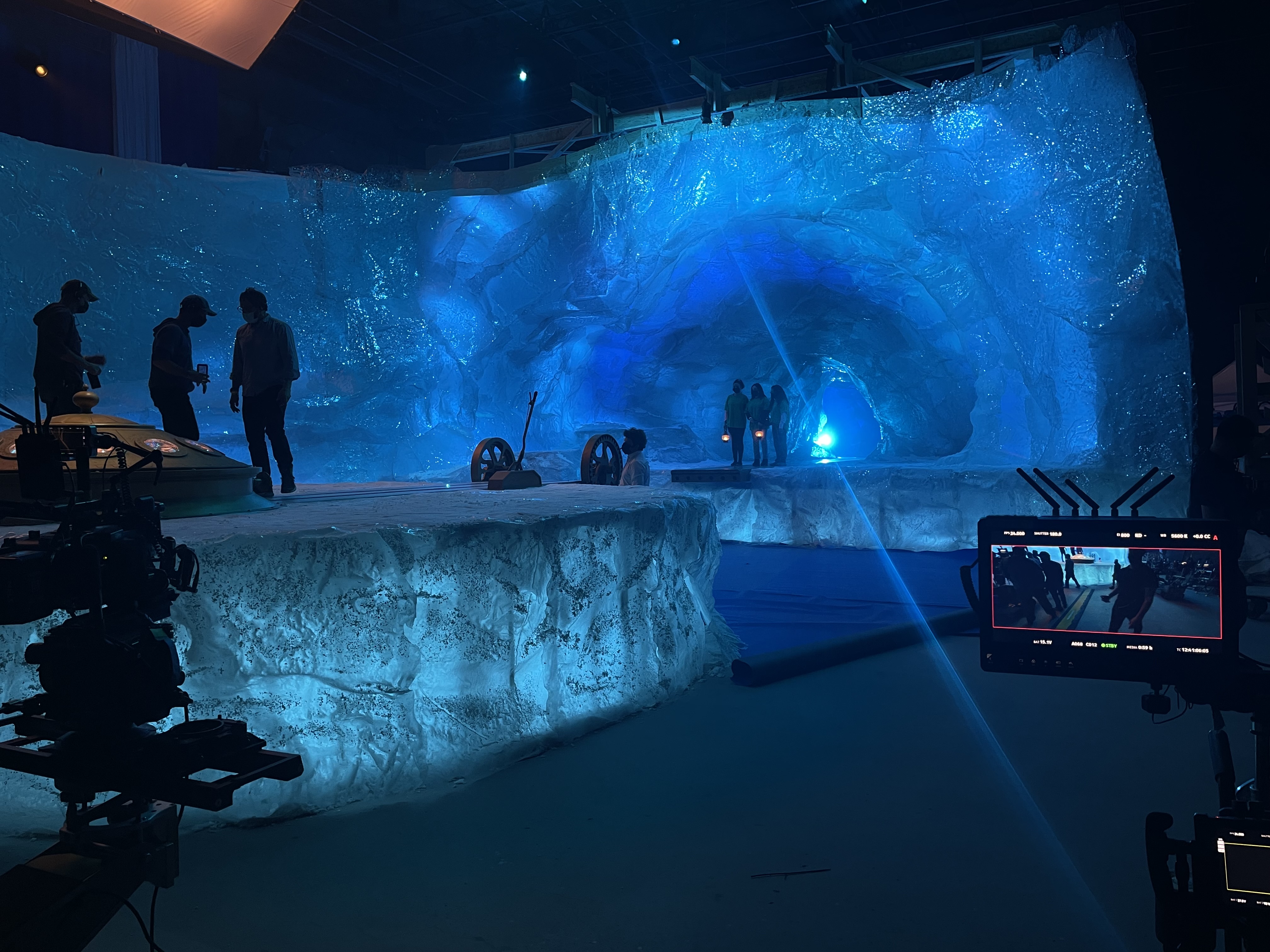 Plateau de tournage avec décor simulant une grotte de glace bleue, plusieurs personnes et caméra de cinéma.