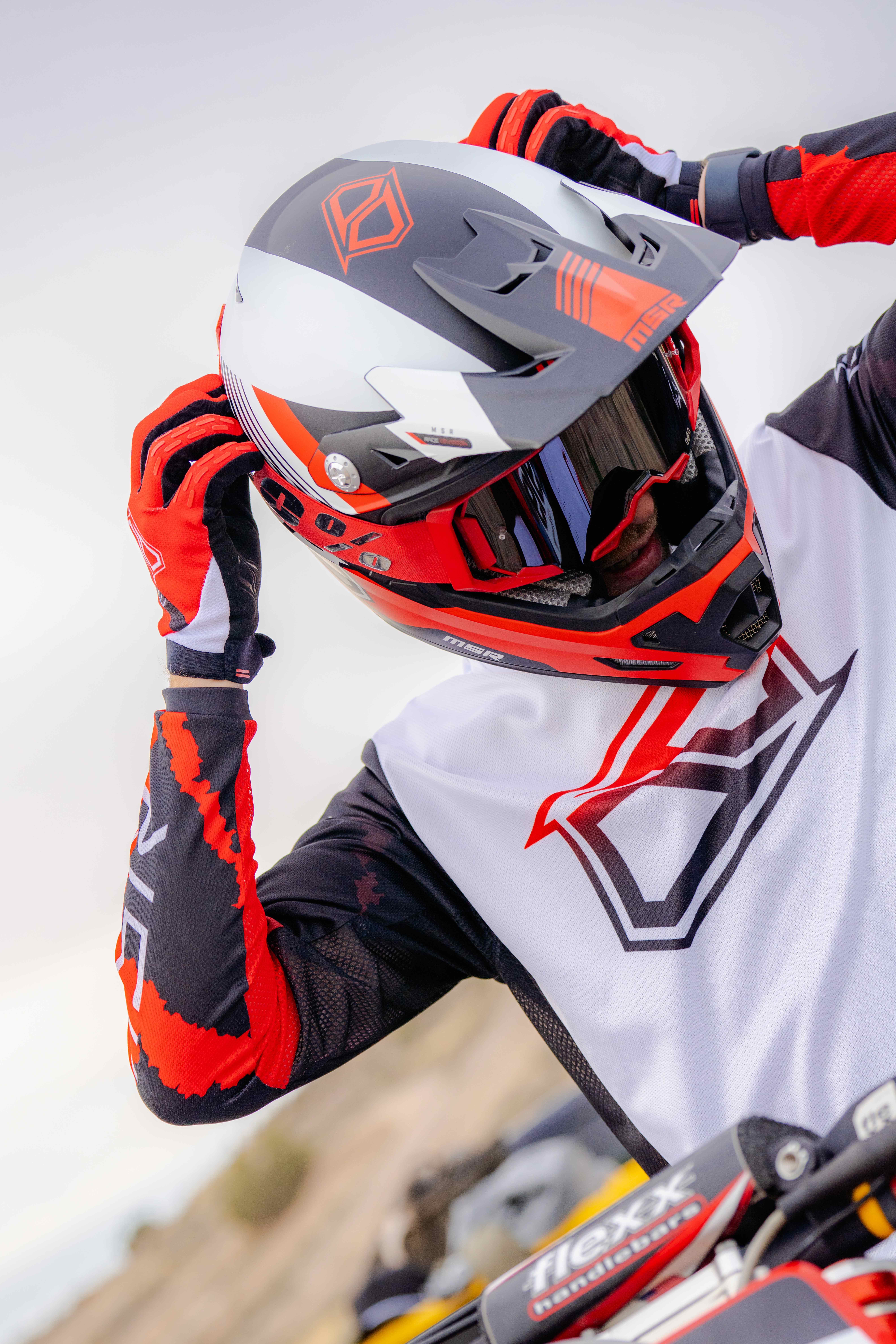 a rider in a black, red and white gear putting on his googles.
