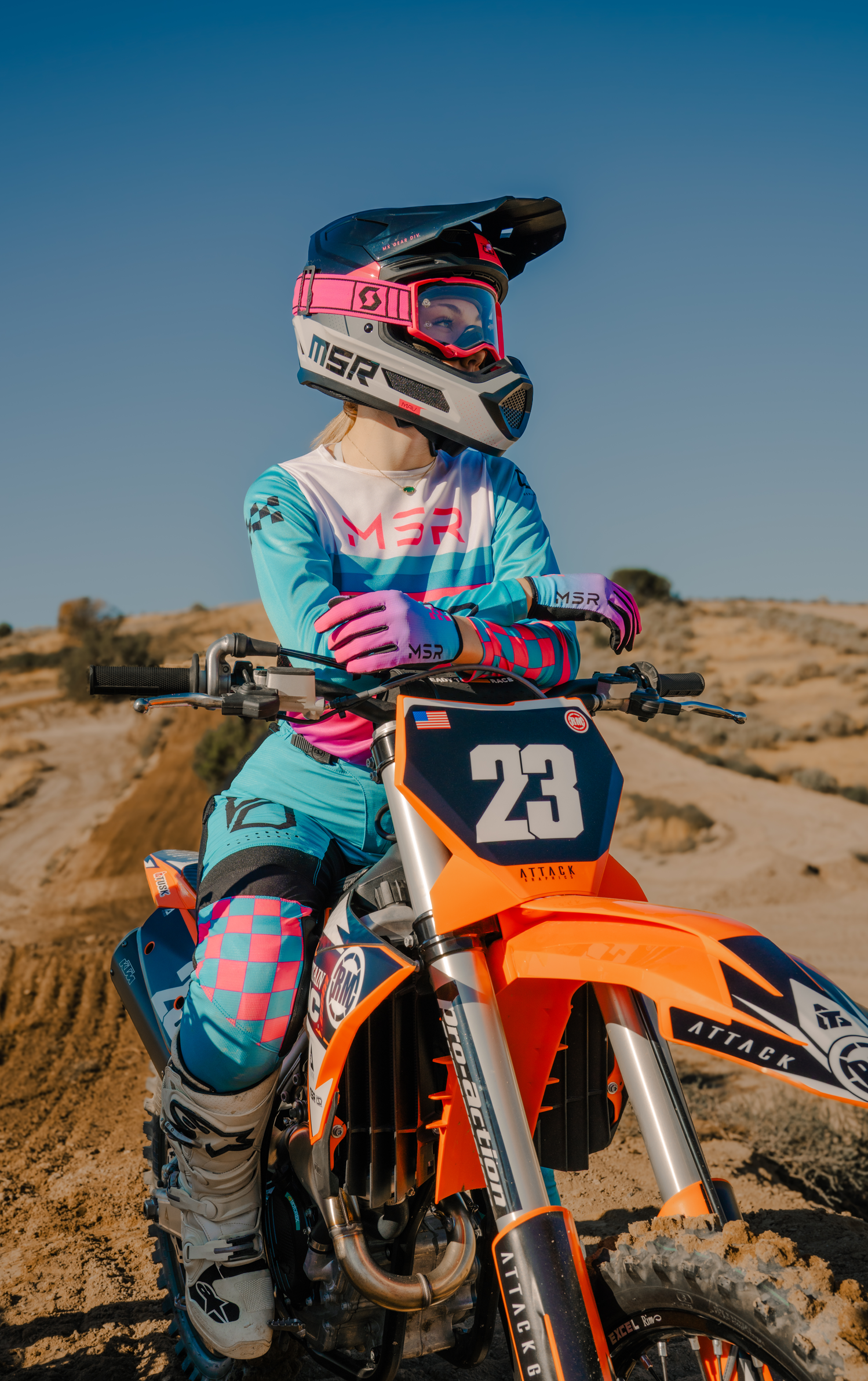 A woman wearing full MSR gear sitting on her bike at the bottom of a hill.