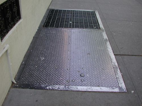 Solid iron cellar doors next to iron grate.
