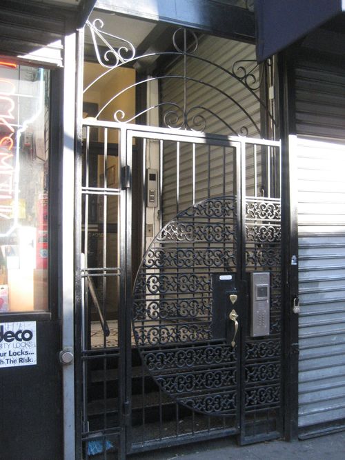Metal security door for entrance of residential apartment building, with decorative fence on both sides and above.