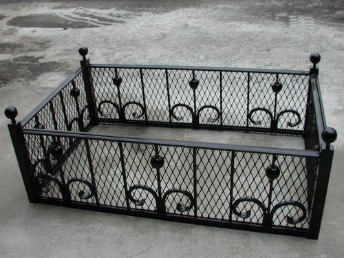 Metal tree pit guard featuring diamond-patterned mesh panels, decorative scrollwork at the bottom, finials on each corner post.