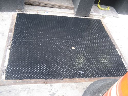 CD19 Flush-mounted, diamond plate steel cellar door with a two-leaf configuration, secured within a metal frame and featuring inset lifting hardware for underground access