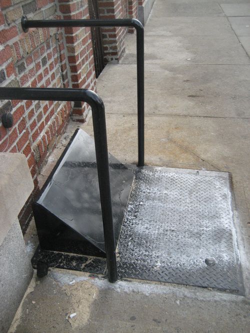 CD25 sidewalk-mounted, diamond plate steel cellar door with an angled protective shroud and safety handrails