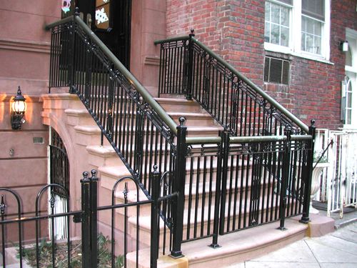 R176 Closely spaced vertical pickets with decorative cast iron collars and scroll elements, topped with a rounded brass cap rail and supported by square newel posts with ornamental finials, all surface-mounted to stone treads and masonry with welded base plates.