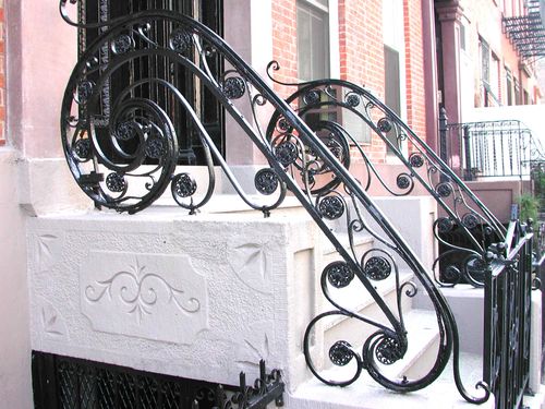 R151 This wrought iron stair railing features a decorative scrollwork design with forged volutes, basket twists, and rosette medallions, mounted to a masonry stoop and finished in a high-gloss black enamel.
