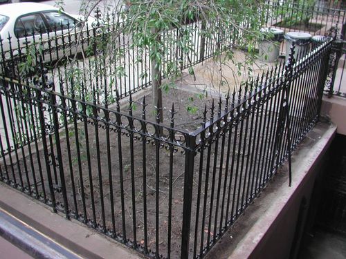 R156 Wrought iron areaway fence constructed with closely spaced square pickets terminating in pressed spear finials, framed by double horizontal rails with a decorative punched circle band, and anchored to a masonry curb