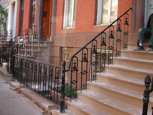 R158 Featuring forged pickets with alternating spear and urn finials, decorative cast-iron collars and rings, curved knuckle details at mid-height, and terminating in newel posts with acorn finials, all anchored into brownstone treads and curb.