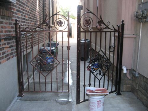 DG164 Double door gate featuring vertical pickets with decorative collars, diamond-patterned scroll insets, and elaborate forged scrollwork with floral rosettes along the arched top rails, all mounted to square steel posts with welded base plates