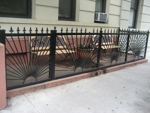 R196 Fence features a repeated sunburst or fanburst design with radial steel pickets anchored in semicircular base plates, topped with alternating spear-point and ball finials, and mounted to low masonry curbing