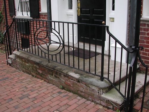 R213 Iron railing for a double return exterior staircase features evenly spaced vertical pickets with an ornamental circular scroll medallion with gold ball finials. The railing follows a double-return entry stair configuration. The top rail curves downward and inward to form a finished volute detail.