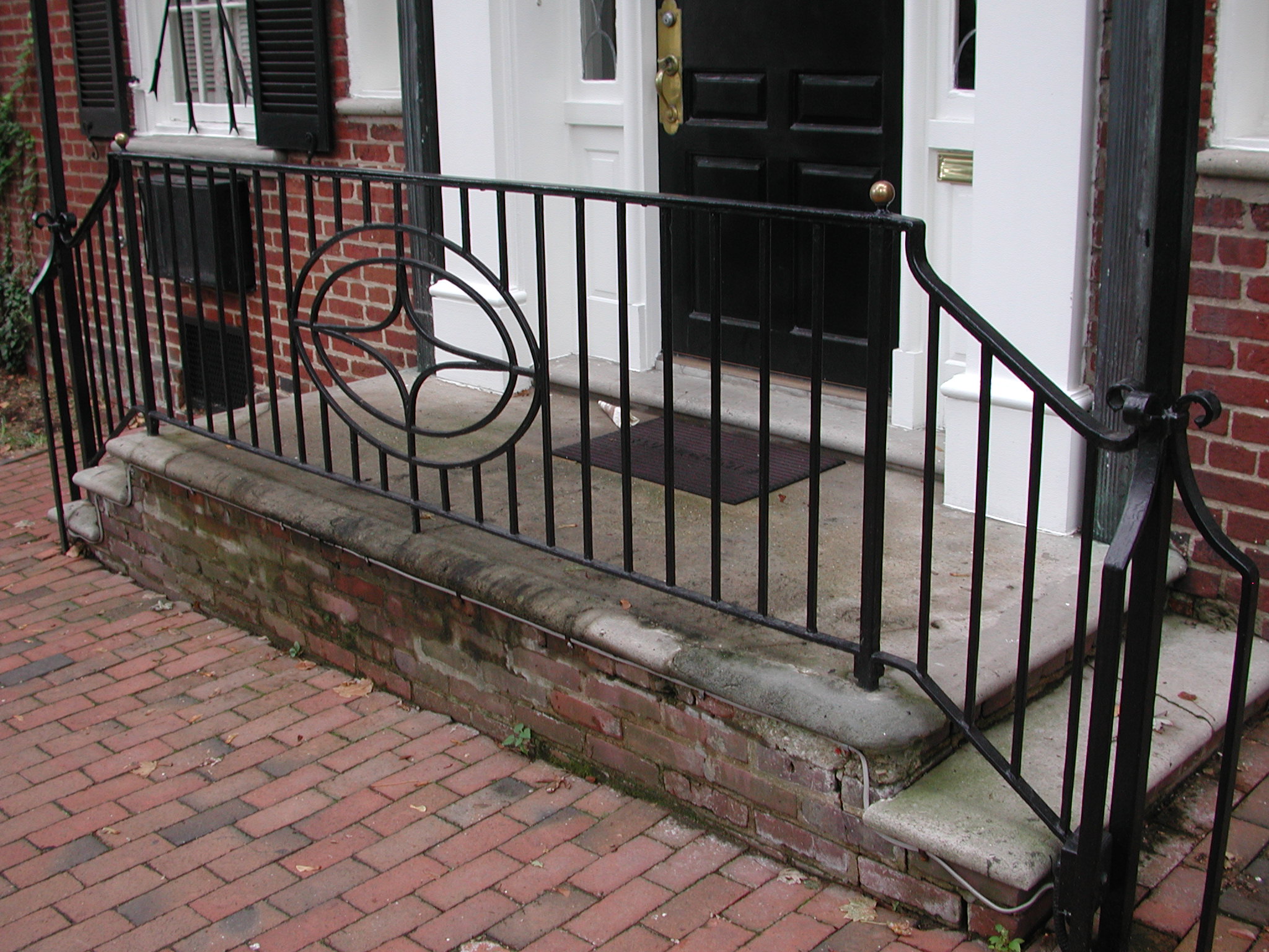 R213 Iron railing for a double return exterior staircase features evenly spaced vertical pickets with an ornamental circular scroll medallion with gold ball finials. The railing follows a double-return entry stair configuration. The top rail curves downward and inward to form a finished volute detail. 