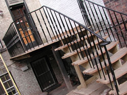 R218 Iron railing features slender vertical balusters with turned spindle details and a smooth continuous top rail that follows the curve of the stair. The top rail curves inward to form a finished volute detail