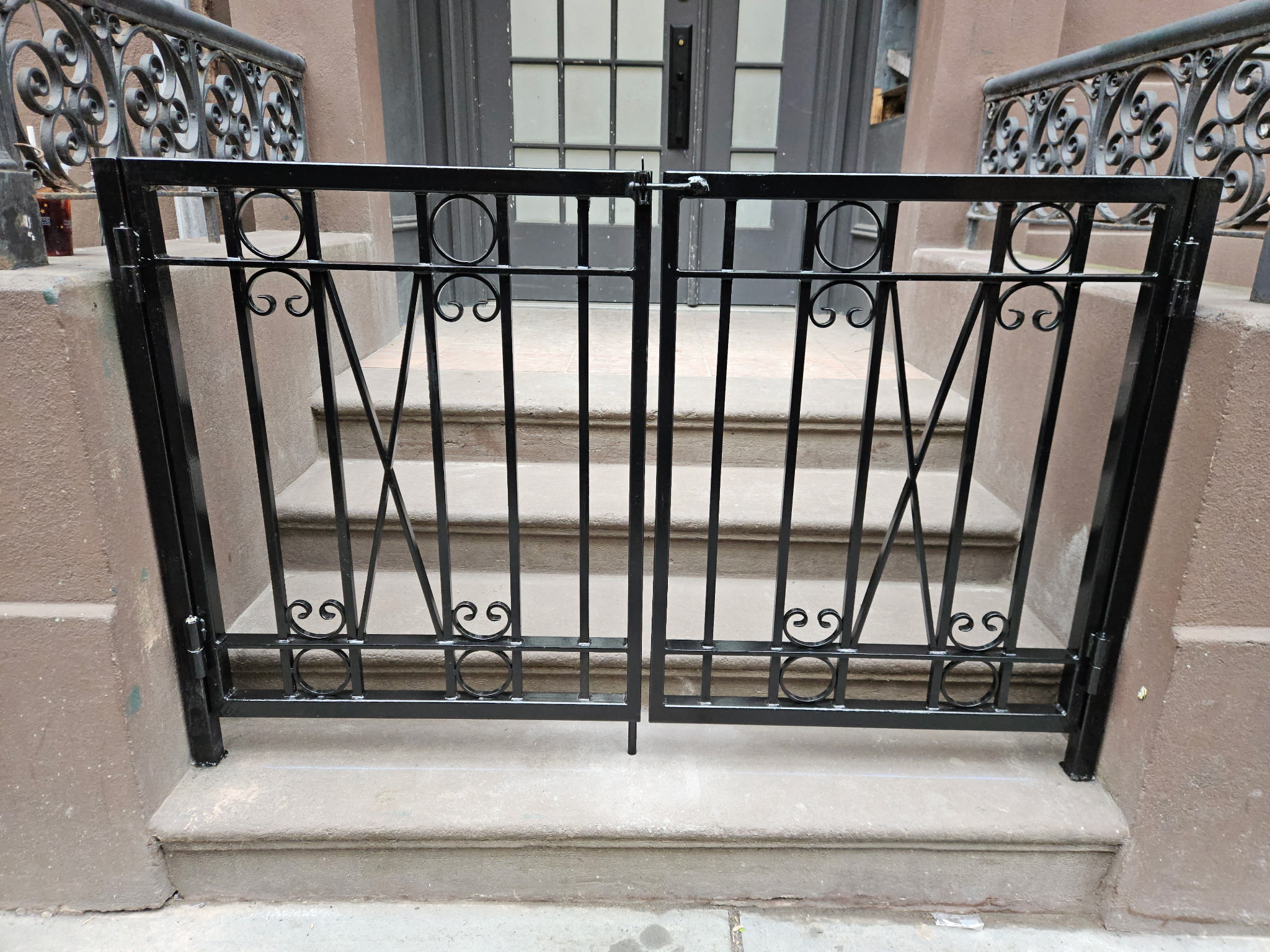 DG176 Custom black steel double-entry gate with vertical pickets, geometric circle details, decorative scrollwork accents, and a secure center latch and floor bolt