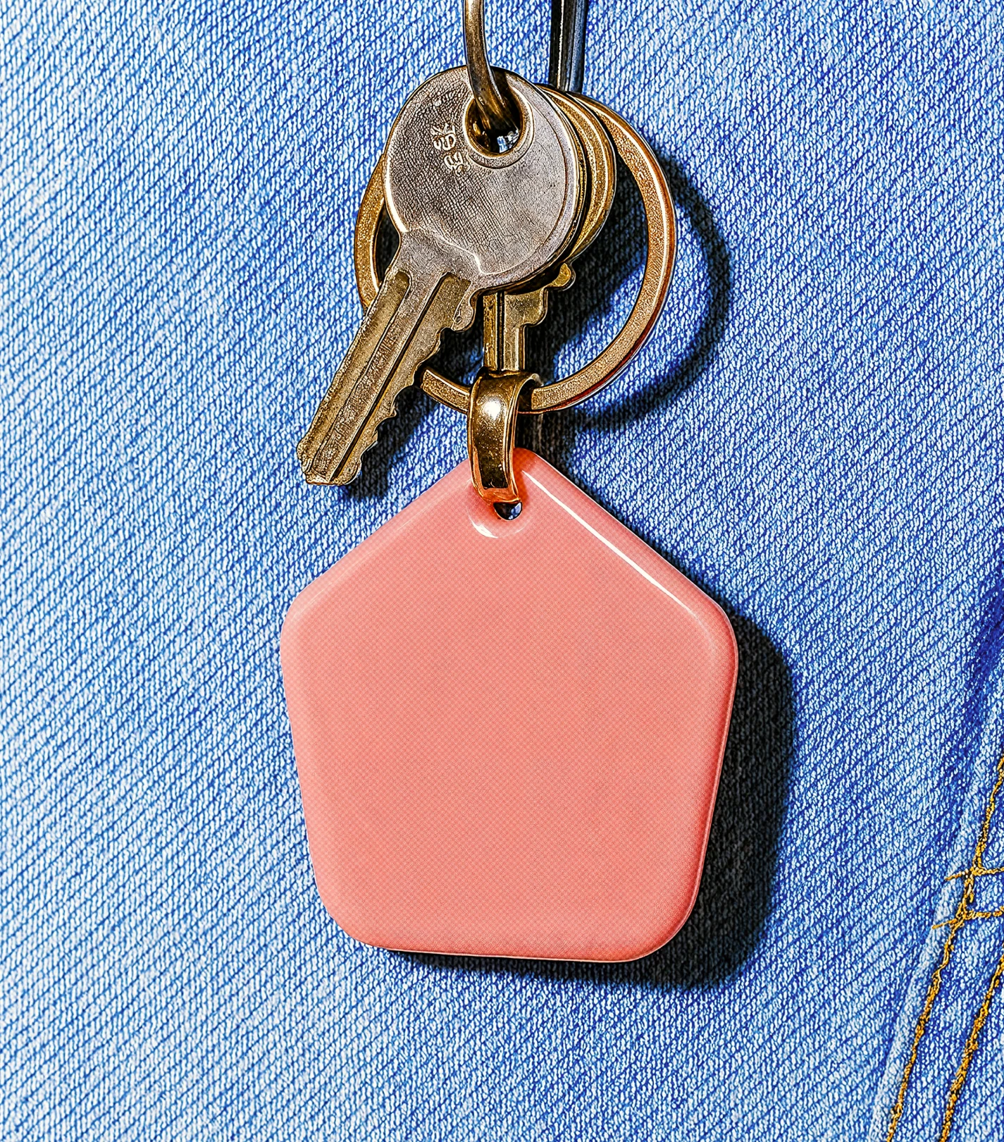 Set of metal keys on a keyring with a blank pink pentagon-shaped keychain on blue denim fabric.