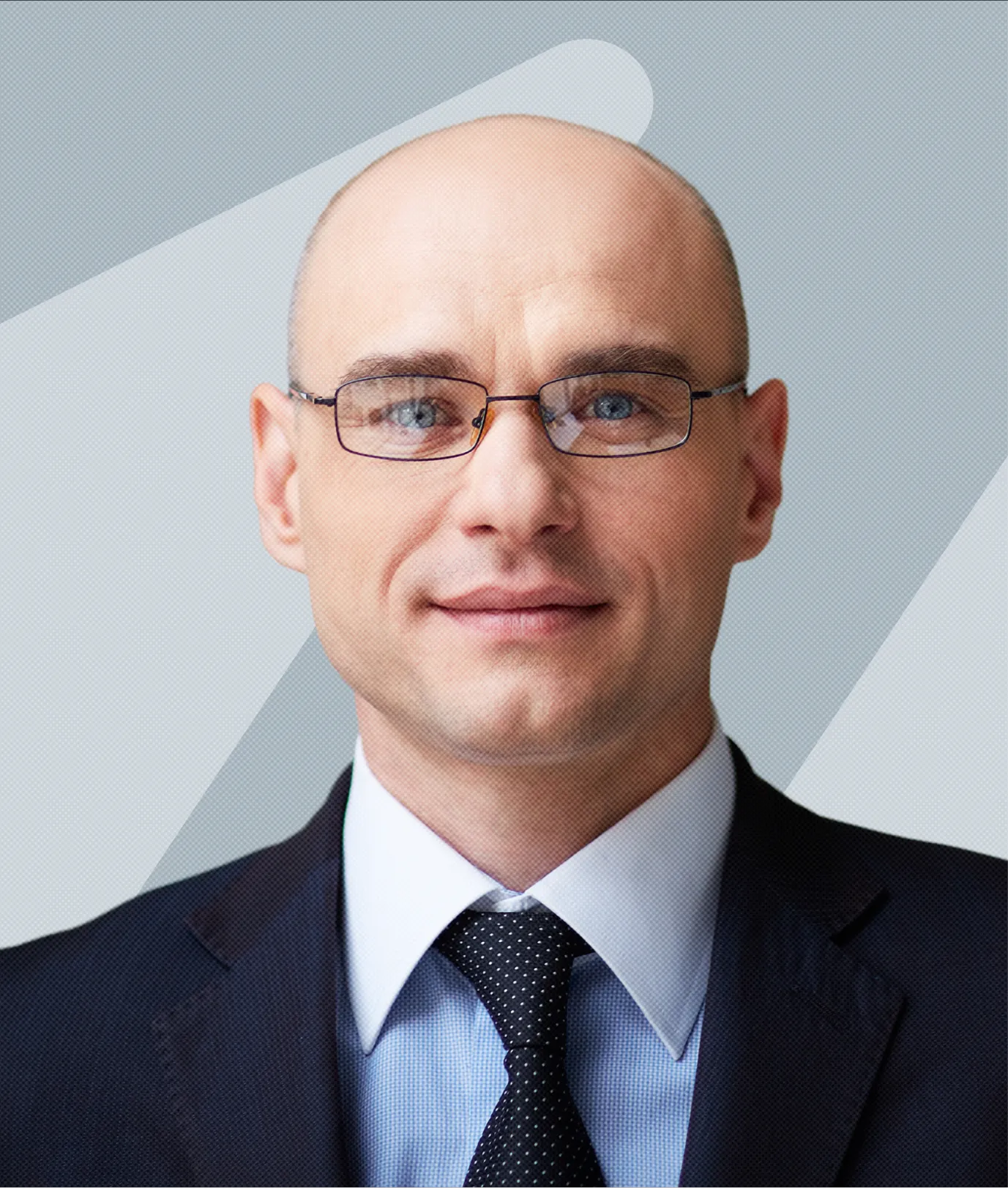 Portrait of a bald man wearing glasses, a dark suit, white shirt, and black polka-dot tie, against a light gray background with abstract shapes.