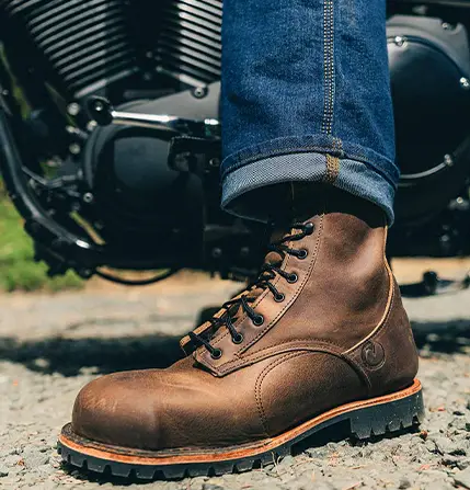 Close-up of a brown leather ORIGIN USA work boot beside a motorcycle.