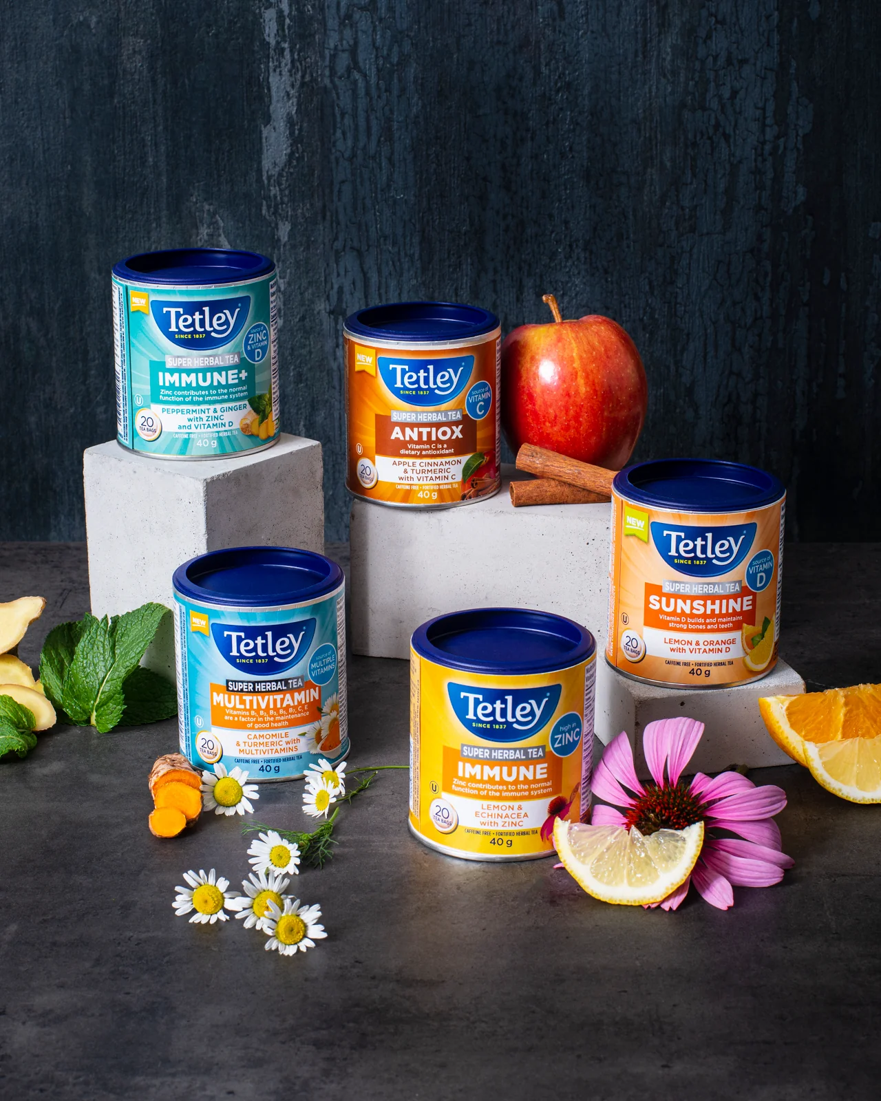 Assortment of Tetley Super Herbal Tea canisters surrounded by fruit, flowers, and spices.