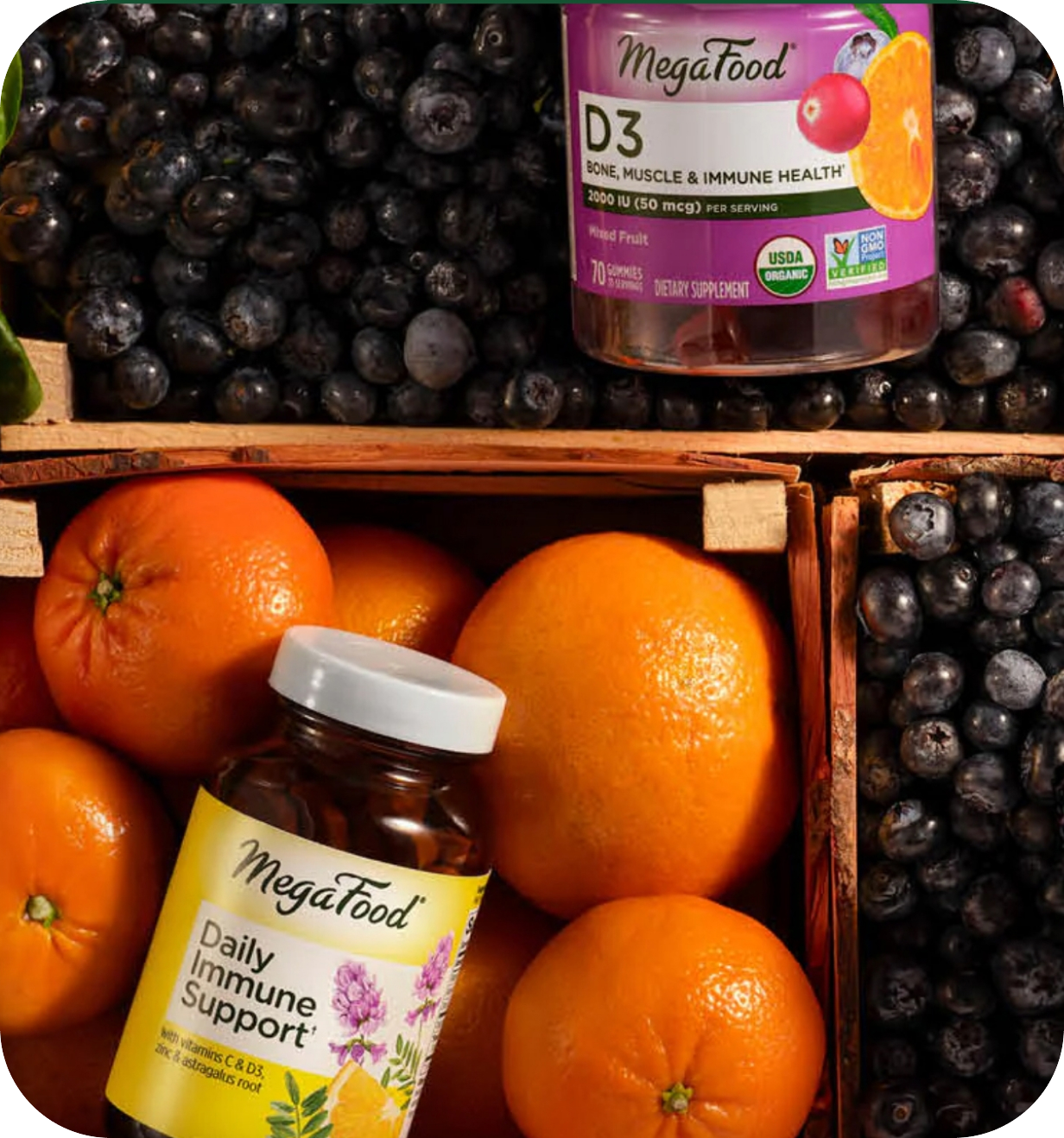 MegaFood vitamin bottles surrounded by fresh oranges and blueberries in a wooden crate.