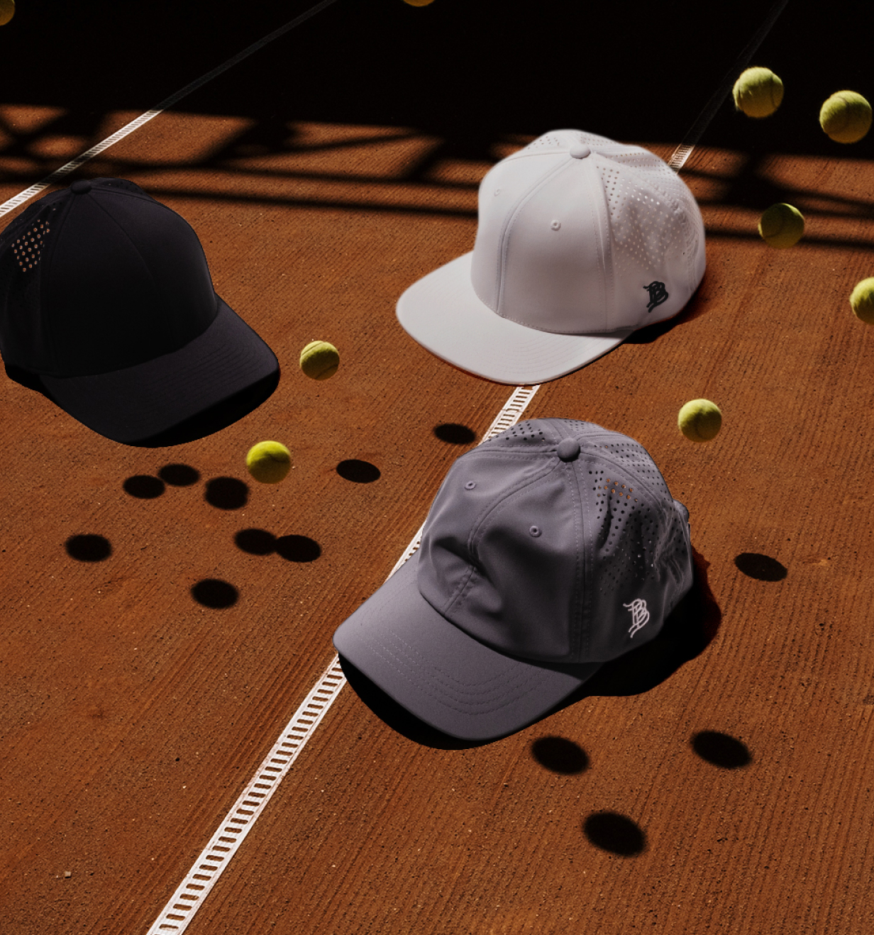 Three Branded Bills baseball caps displayed on a clay tennis court surrounded by tennis balls.
