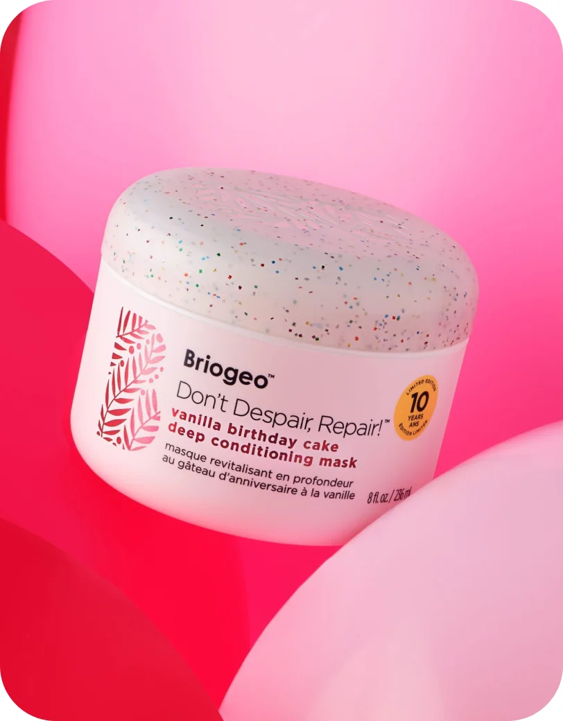 Briogeo Don't Despair, Repair! vanilla birthday cake deep conditioning mask jar on a pink background with balloons.