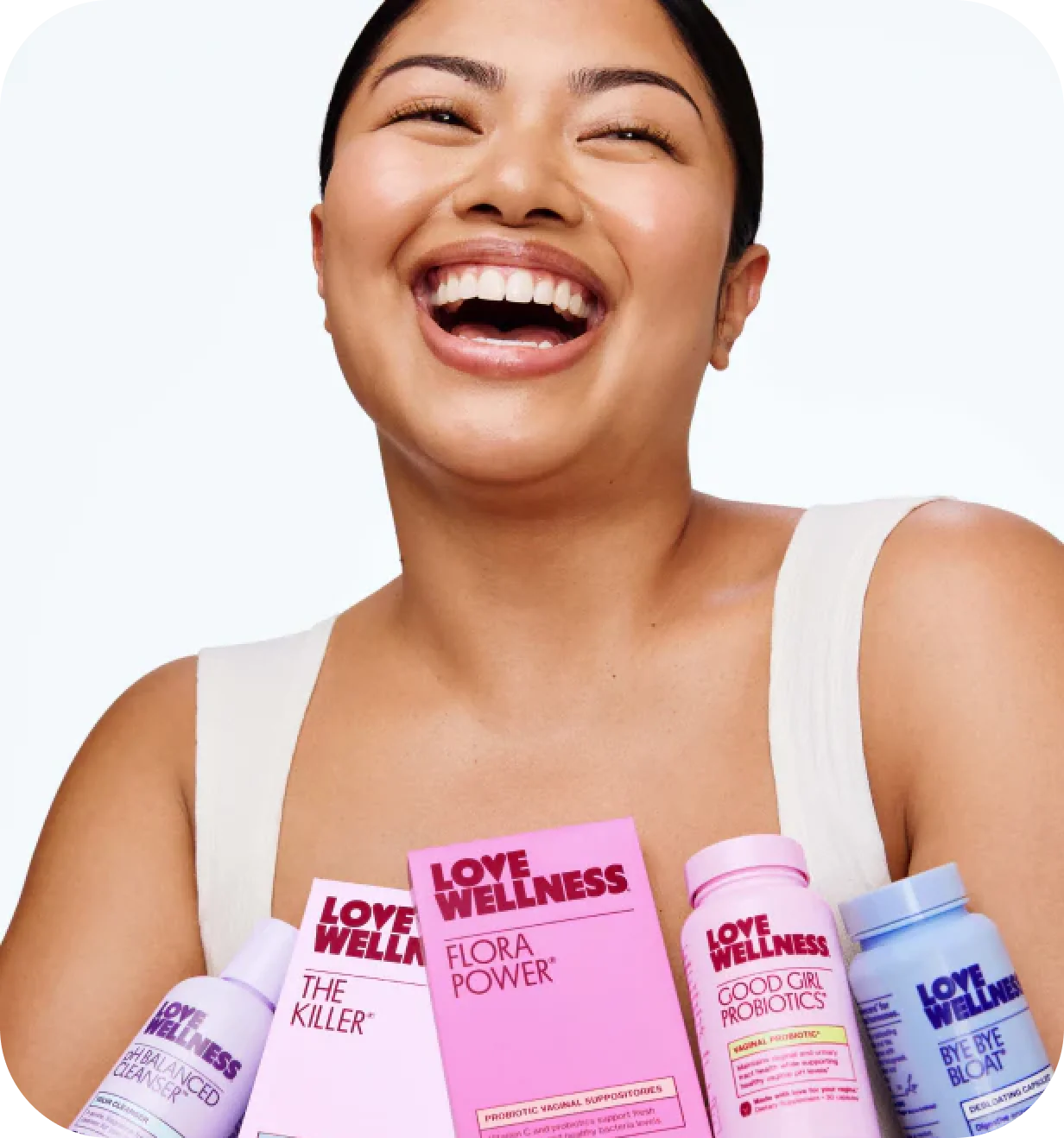 Laughing woman holding an assortment of Love Wellness supplement and skincare products.