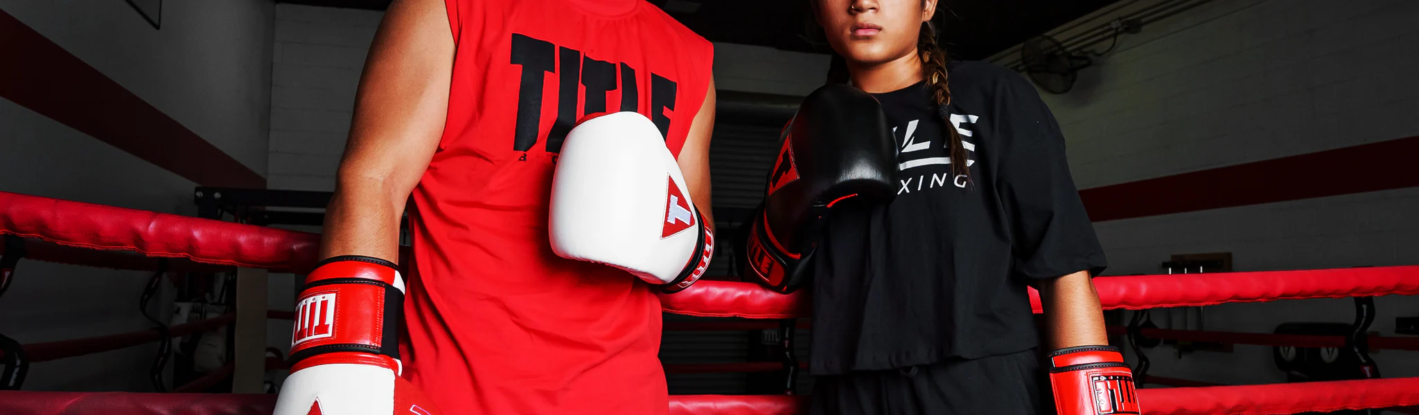 Two boxers wearing TITLE Boxing apparel and gloves standing in the corner of a red-roped ring.