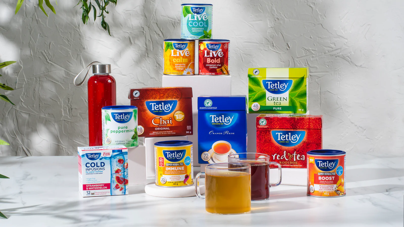 Assortment of Tetley tea boxes and canisters with two glass mugs of brewed tea.