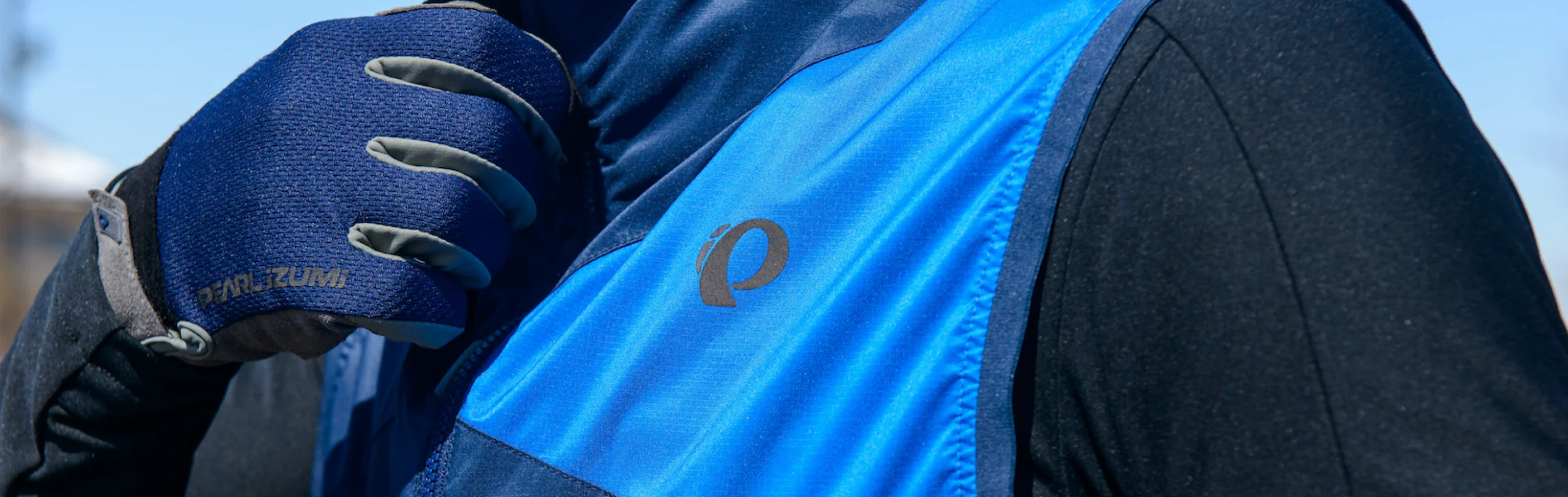 Cyclist zipping a blue PEARL iZUMi vest while wearing matching PEARL iZUMi gloves.