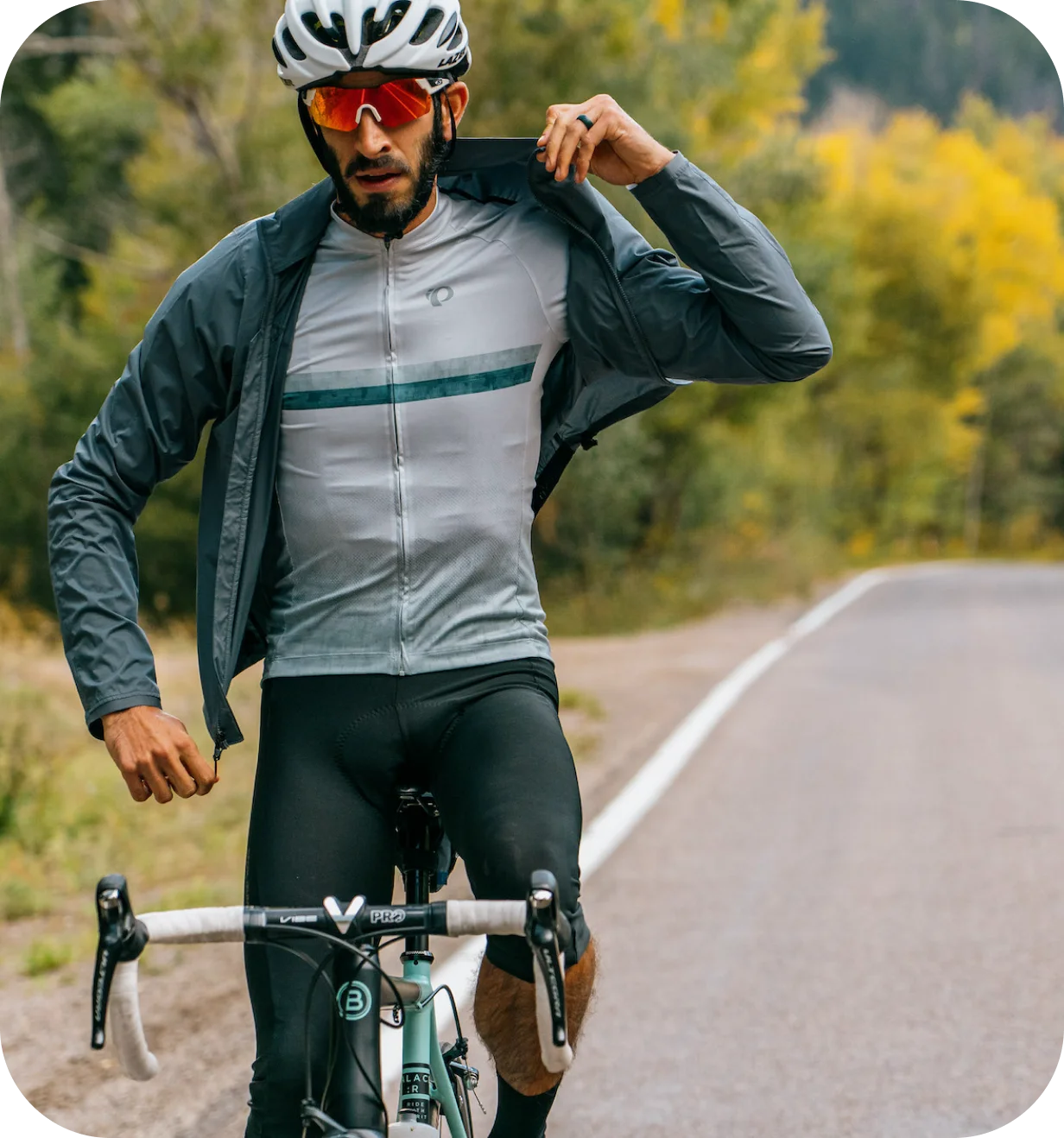 PEARL iZUMi lifestyle photo of a cyclist in a jersey and packable jacket on a forest road.
