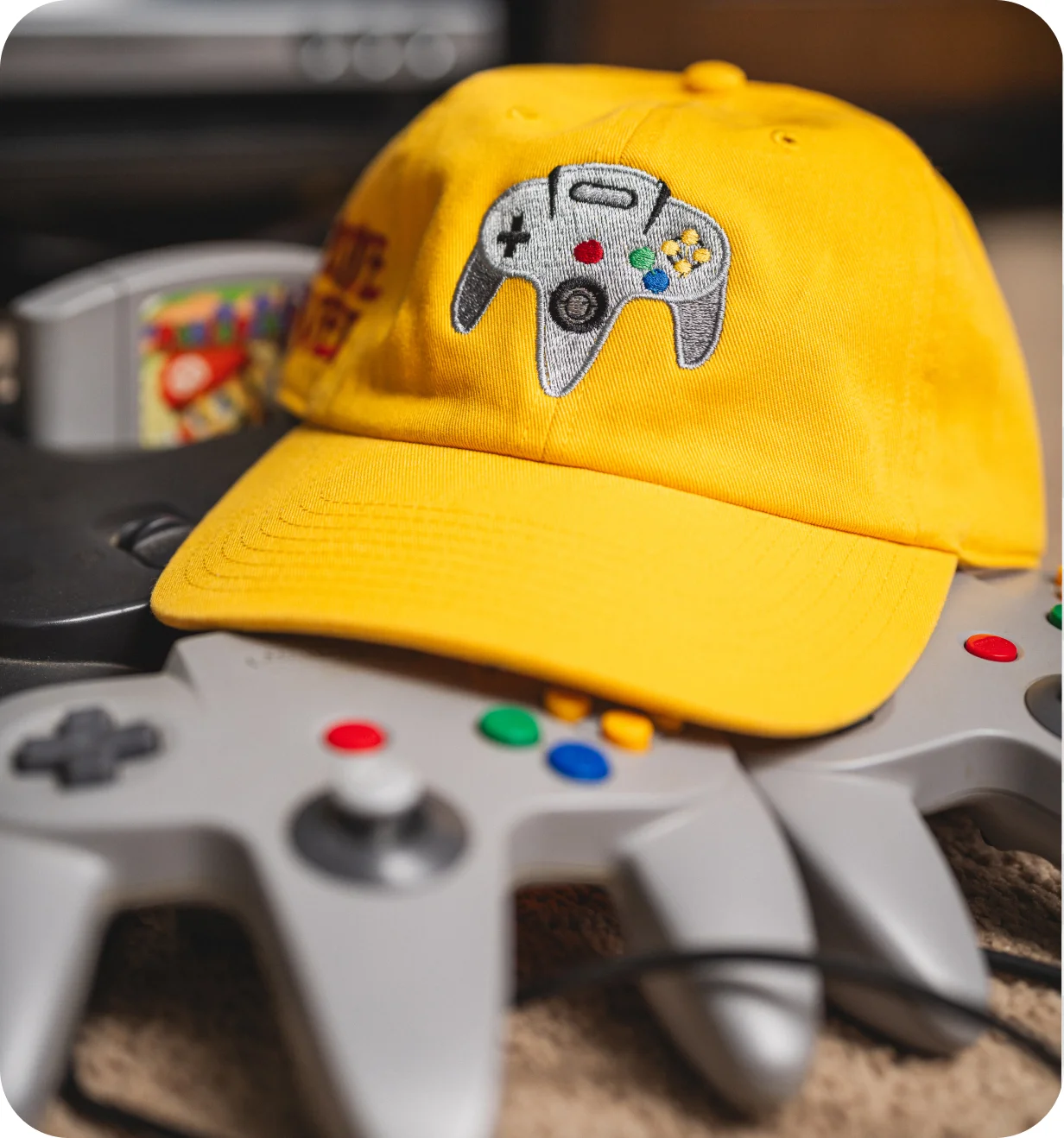 Yellow Custom Lids dad hat with an embroidered N64 controller resting on a Nintendo 64 console and controller.