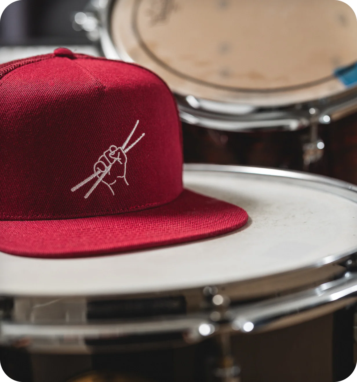 Red Custom Lids snapback with an embroidered drumsticks design sitting on a snare drum.